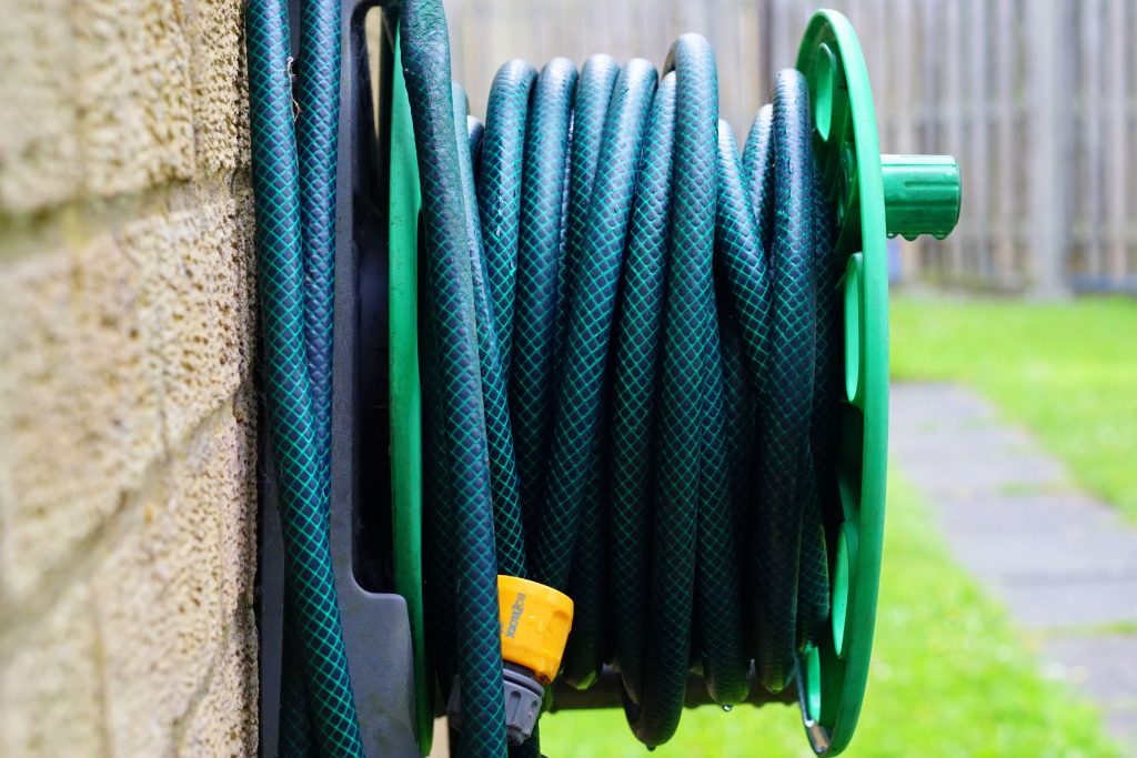Green garden hose wound on a wall-mounted hose reel