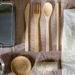 Stainless steel lunch box with bamboo cutlery, a glass jar of walnuts and an apple on a cloth napkin