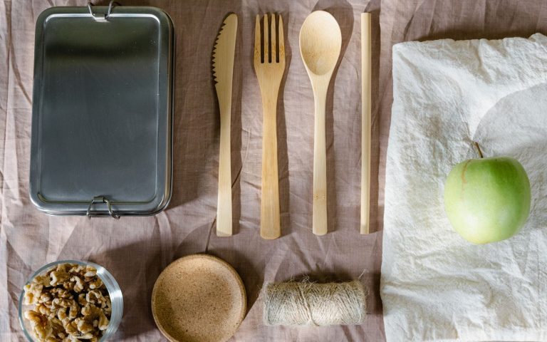 Stainless steel lunch box with bamboo cutlery, a glass jar of walnuts and an apple on a cloth napkin
